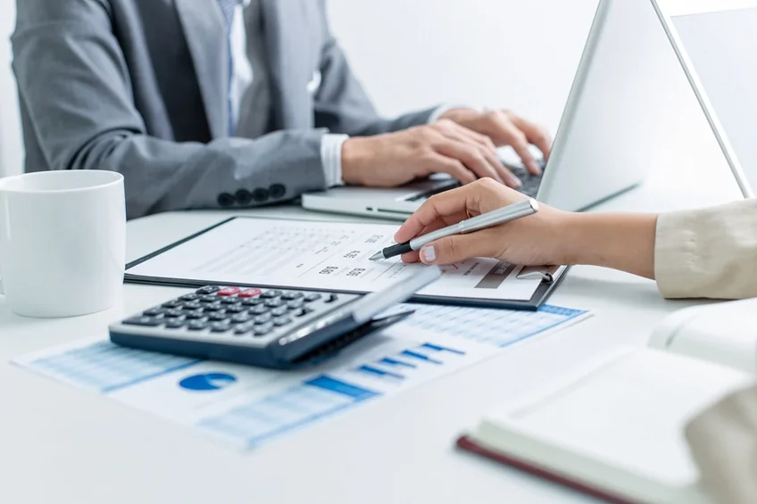 A laptop, calculator and financial charts on a desk.