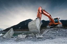 An excavator bucket at work on a rock face.