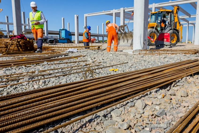 Site workers in safety gear beside steel reinforcement bars.