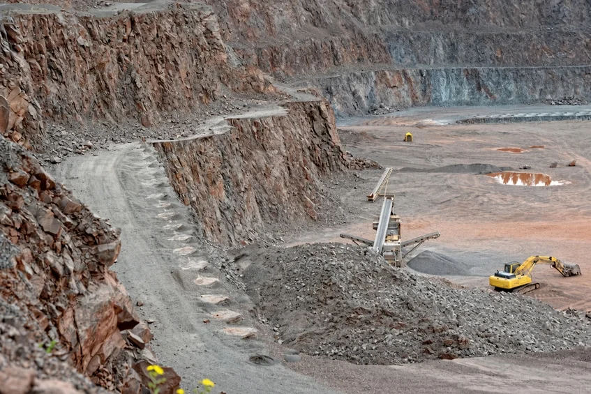 Terraced benches of an open-cut quarry with a working excavator.
